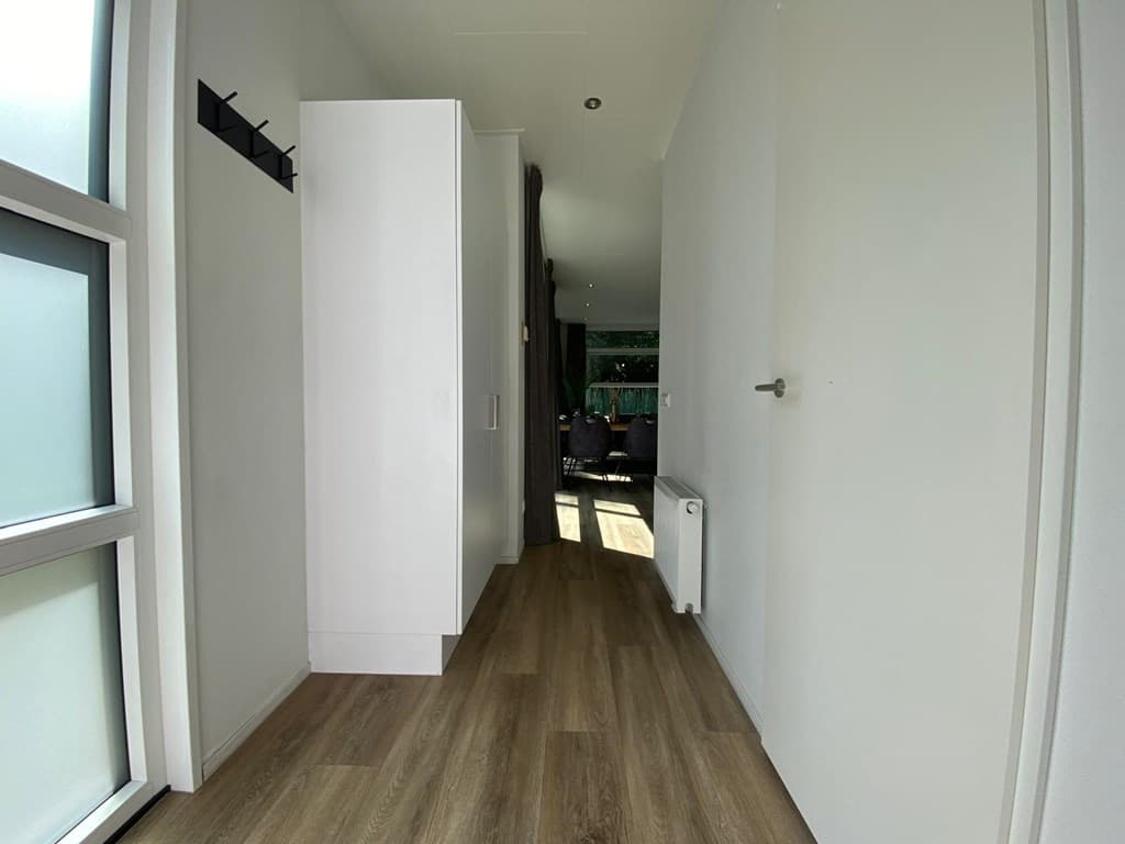 In het zichtbare interieur zijn een gang met een kast, houten vloer en toegang naar een lichte woonkamer.