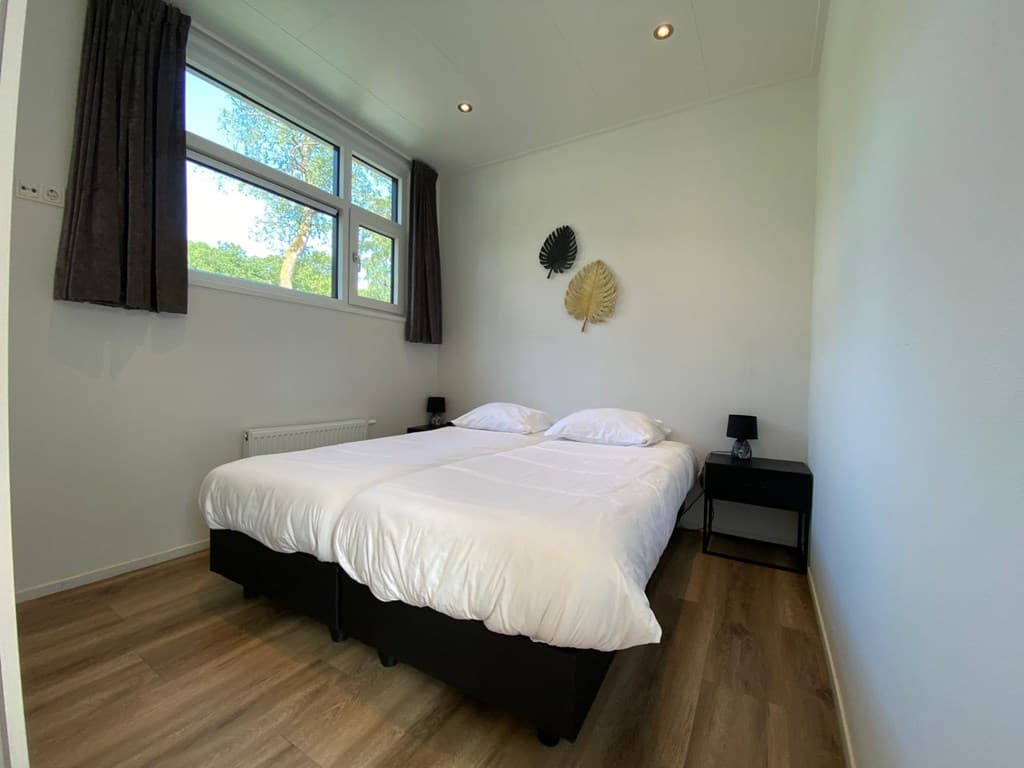 Sfeervolle slaapkamer met twee eenpersoonsbedden, nachtkastjes en grote ramen met uitzicht op groen.