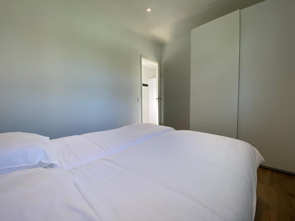 Slaapkamer met twee eenpersoonsbedden en een kast, deur naar een andere ruimte zichtbaar op de achtergrond