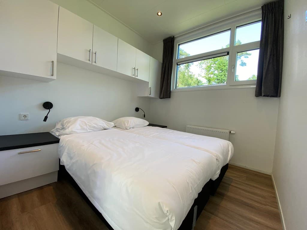 Slaapkamer met twee eenpersoonsbedden, wandkasten, bedside lamps en een raam met uitzicht op bomen.