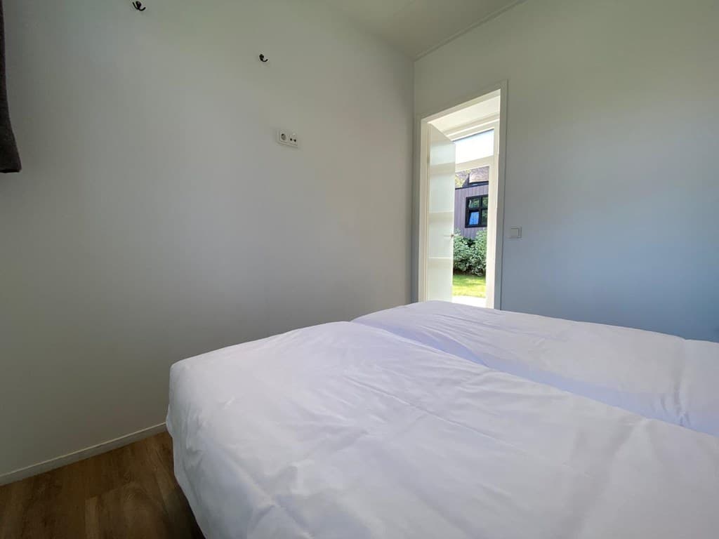 Slaapkamer met twee eenpersoonsbedden en deur naar buiten, lichte muren en houten vloer.