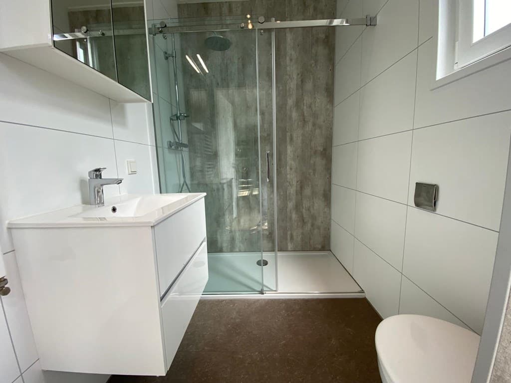 Moderne badkamer met inloopdouche, wastafel en toilet, lichte muren en donkere vloer.