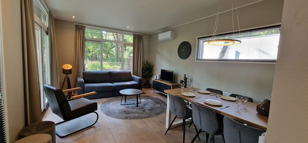 Moderne woonkamer met zithoek, eettafel en grote ramen met uitzicht op de natuur