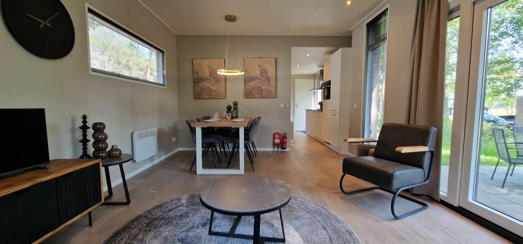 Ruime woonkamer met eethoek, zithoek en grote ramen die uitzicht bieden op de groene omgeving.