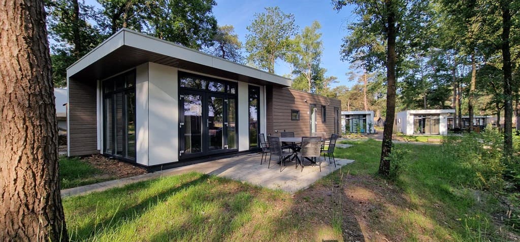 Moderne vakantiewoningen in een bosrijke omgeving met terras en eetset op een betegeld oppervlak.