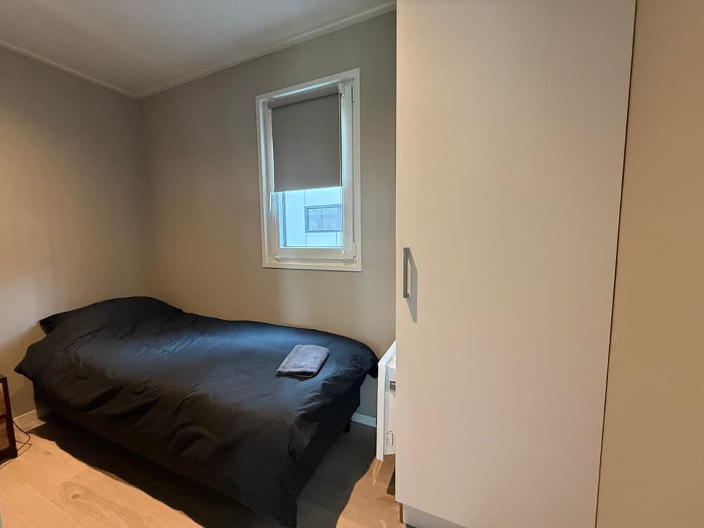 Slaapkamer met éénpersoonsbed, witte kast en raam met een verduisterend raamdecoratie.