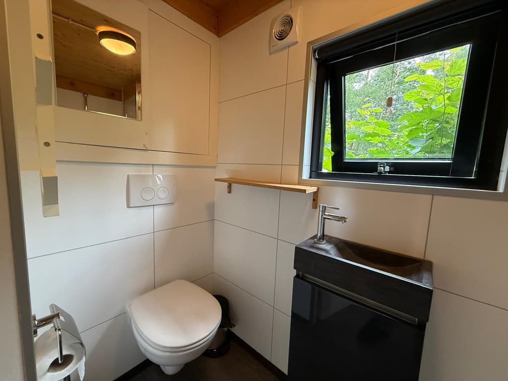 Kleine badkamer met toilet, wastafel en een raam met uitzicht op groene bomen.