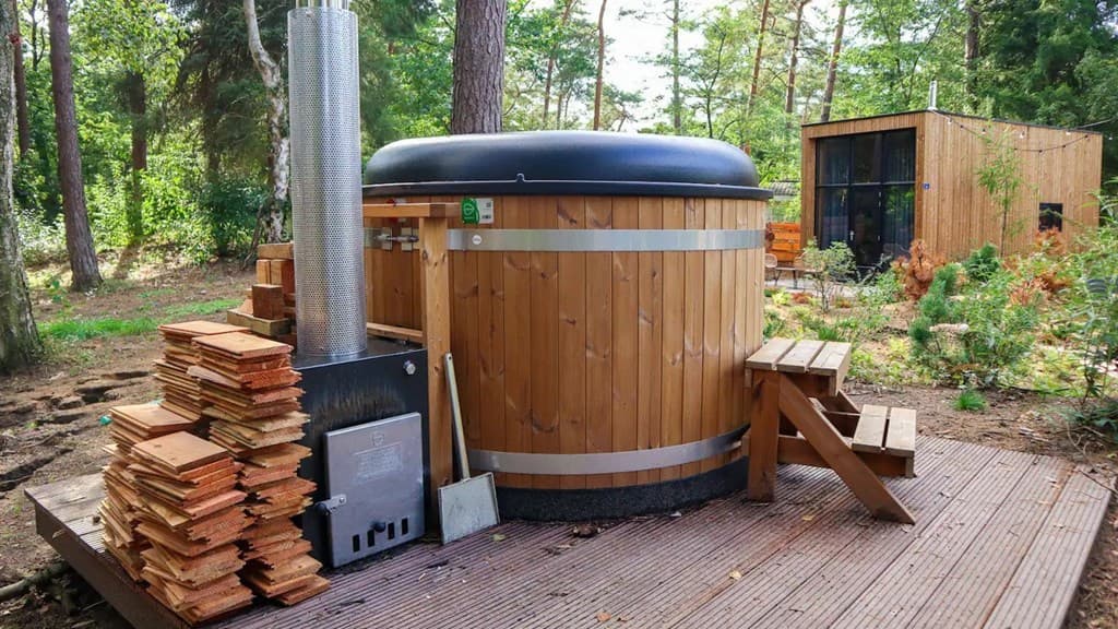 Houten wellnessbad met stenen en een houten platform omringd door bosachtige omgeving