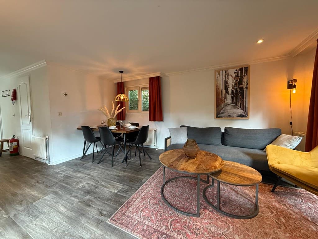 Woonkamer met grijze bank, eettafel, zwarte stoelen, een schilderij en een geel accent in het interieur