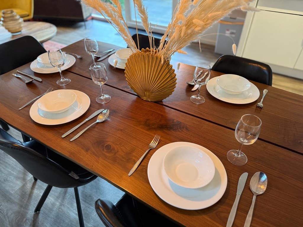 Eettafel met zes plaatsen, witte borden en glazen, en een vaas met decoratieve takken in het midden.
