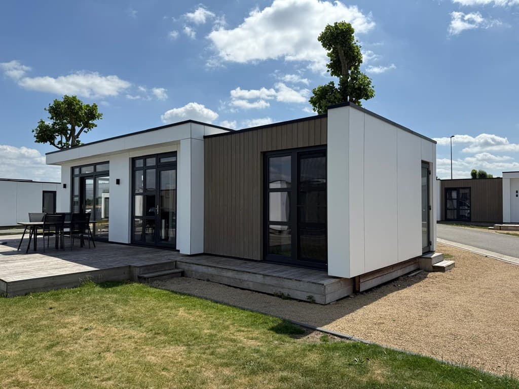 Moderne vakantiewoning met lichte gevel en houten accenten, omringd door een grasveld en blauwe lucht met wolken.