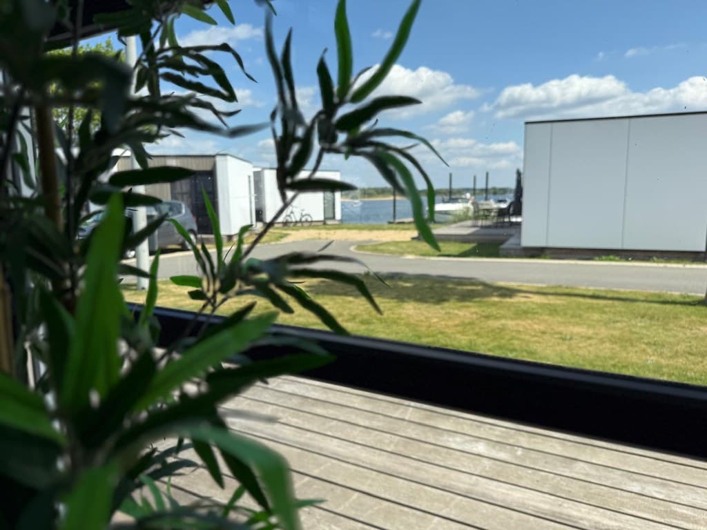 Uitzicht vanaf een houten terras met groen, zicht op het water en villas aan de andere kant van het pad.
