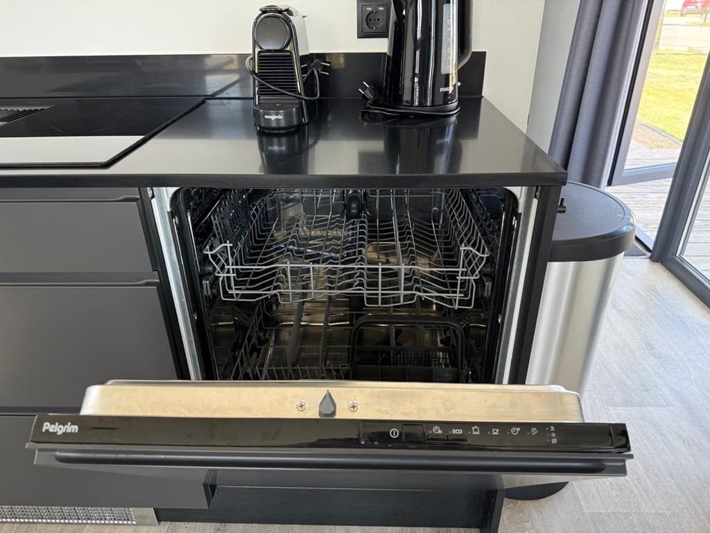 Ingebouwde vaatwasser met open deur in een moderne keuken met zwarte afwerking en apparatuur.