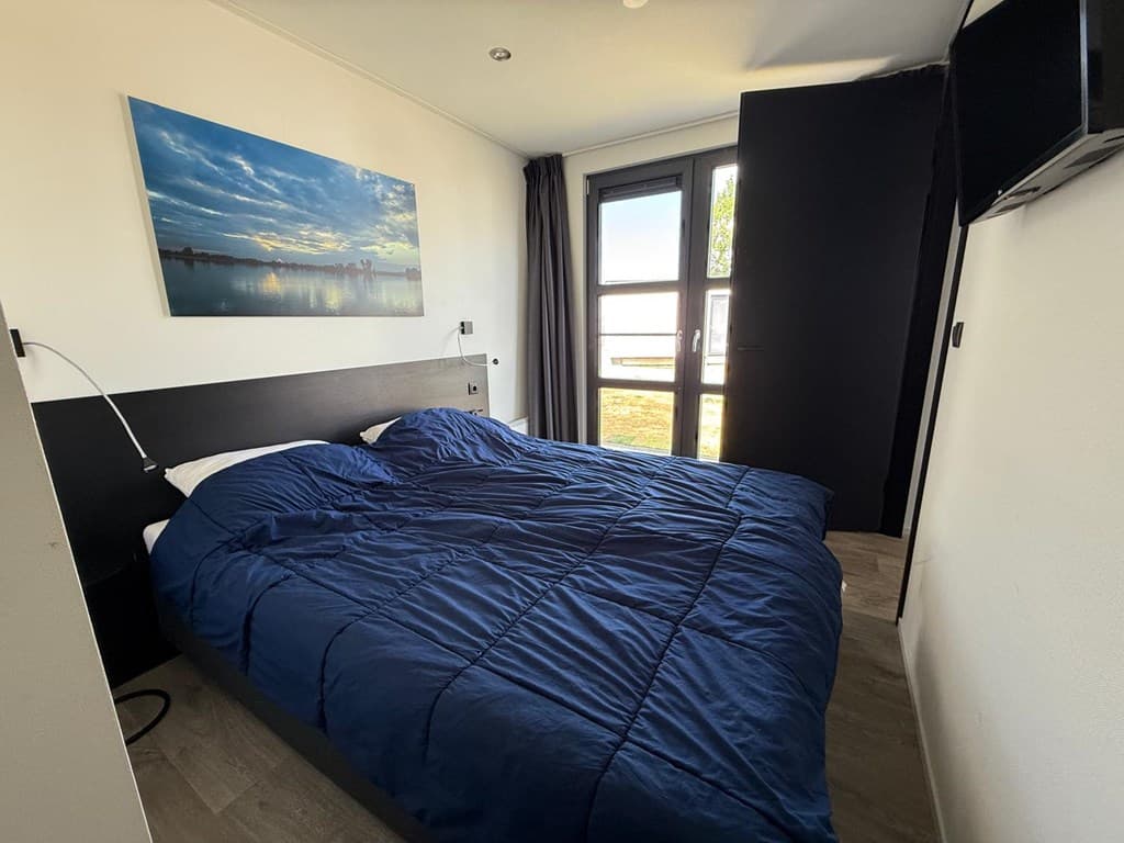 Slaapkamer met een tweepersoonsbed, raam met uitzicht en een tv aan de muur.