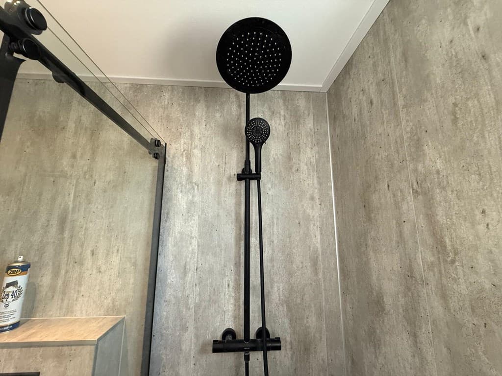 Douche met zwarte regen- en handdouchekop aan een betonachtige wand in een moderne badkamer