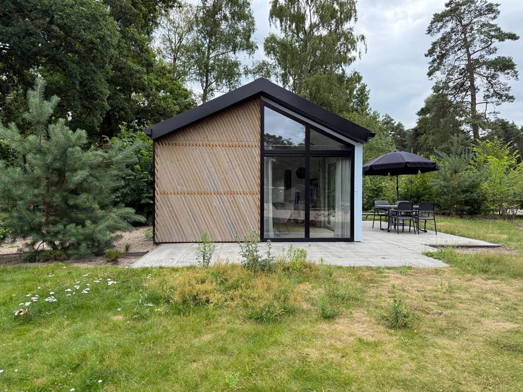Moderne vakantiewoning met glazen gevel en houten panelen, buiten terras met tafel en parasol, omringd door groen