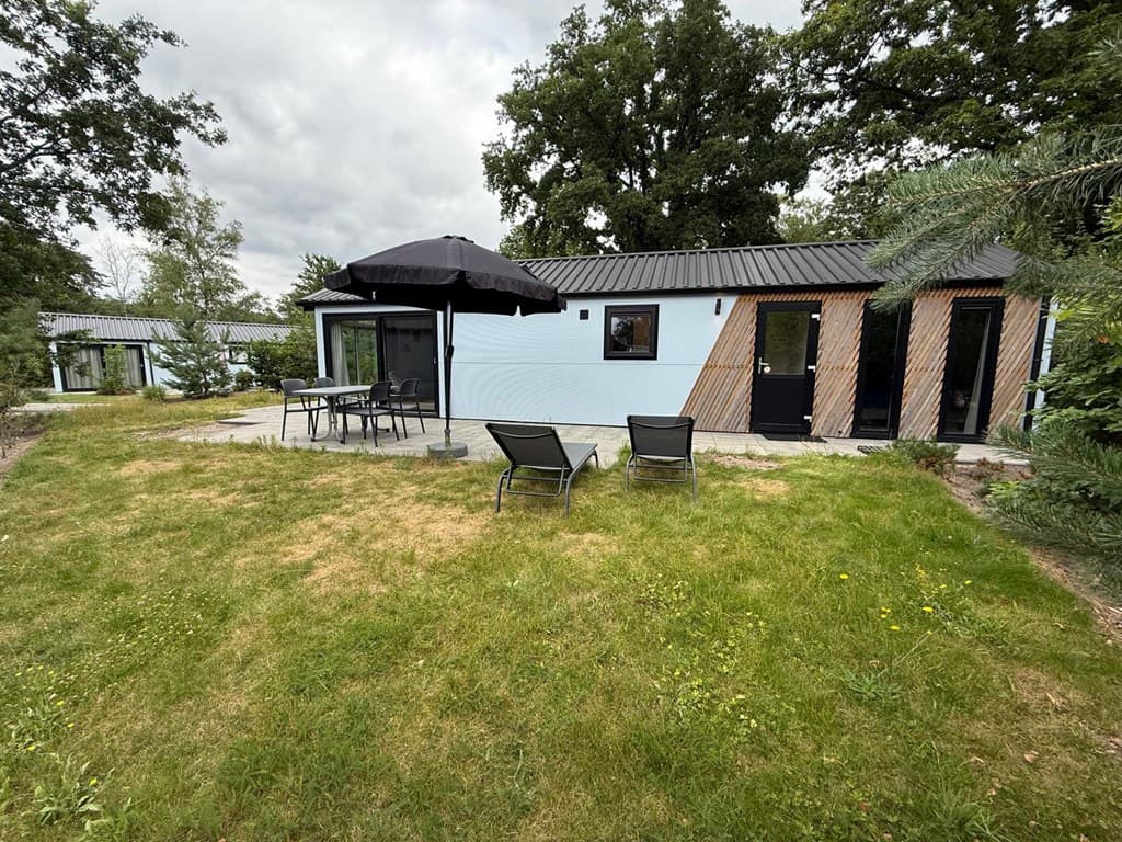 Tuin met gras, terras met stoelen, tafel en parasol bij een modern vakantiehuis in EuroParcs De Hooge Veluwe.