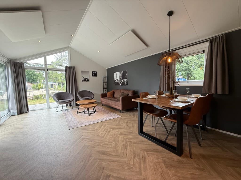 Moderne woonkamer met zithoek, eettafel en grote ramen met uitzicht op de tuin op EuroParcs De Hooge Veluwe.