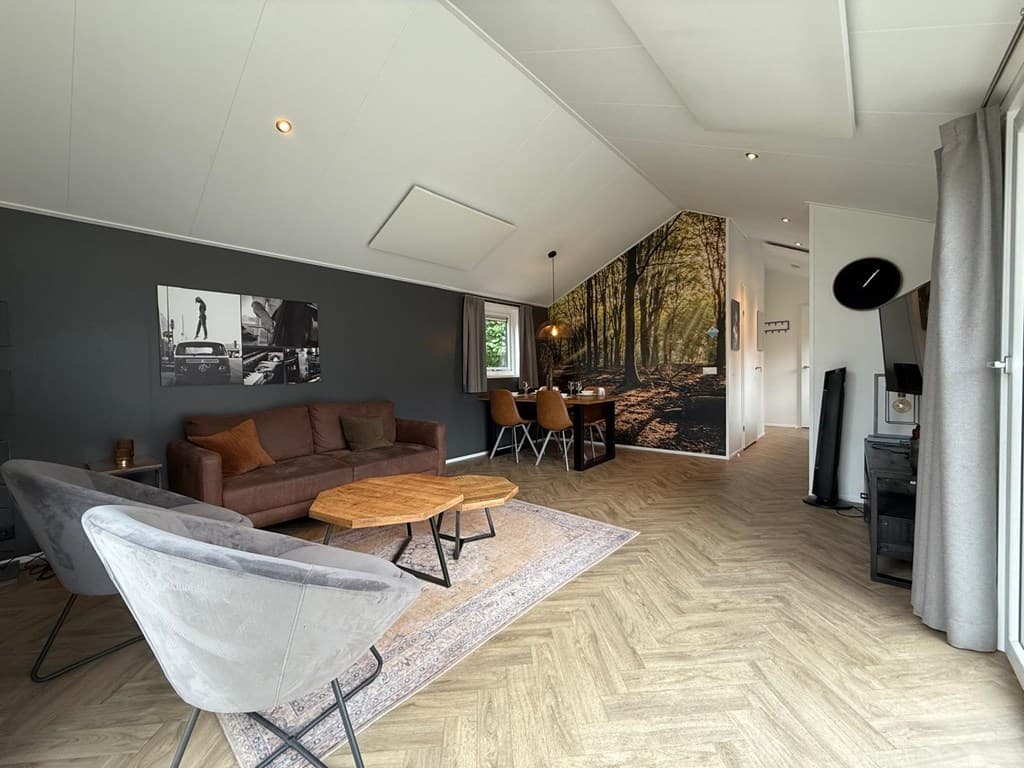 Moderne woonkamer met bank, eettafel en een wanddecoratie van een boslandschap in EuroParcs De Hooge Veluwe.