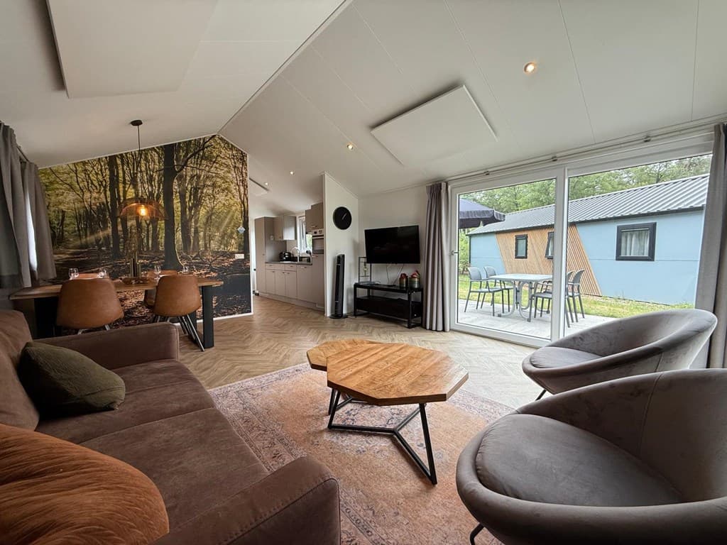 Moderne woonkamer met bank, stoelen, eethoek en grote ramen met uitzicht op buitenruimte en boswanddecoratie