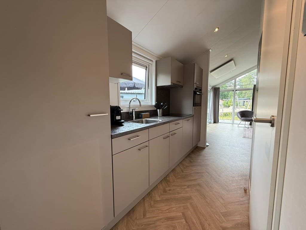 Keuken met lichte kasten en een aanrecht, uitzicht op een open woonkamer met veel natuurlijk licht.