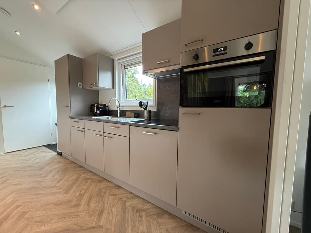 Moderne keuken met aanrecht, kastjes, oven, magnetron en uitzicht op een raam met groen buiten.