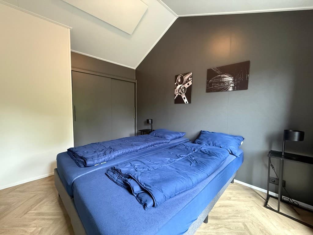 Slaapkamer met twee losse bedden, donkere wand, kleerkast en kunst aan de muur