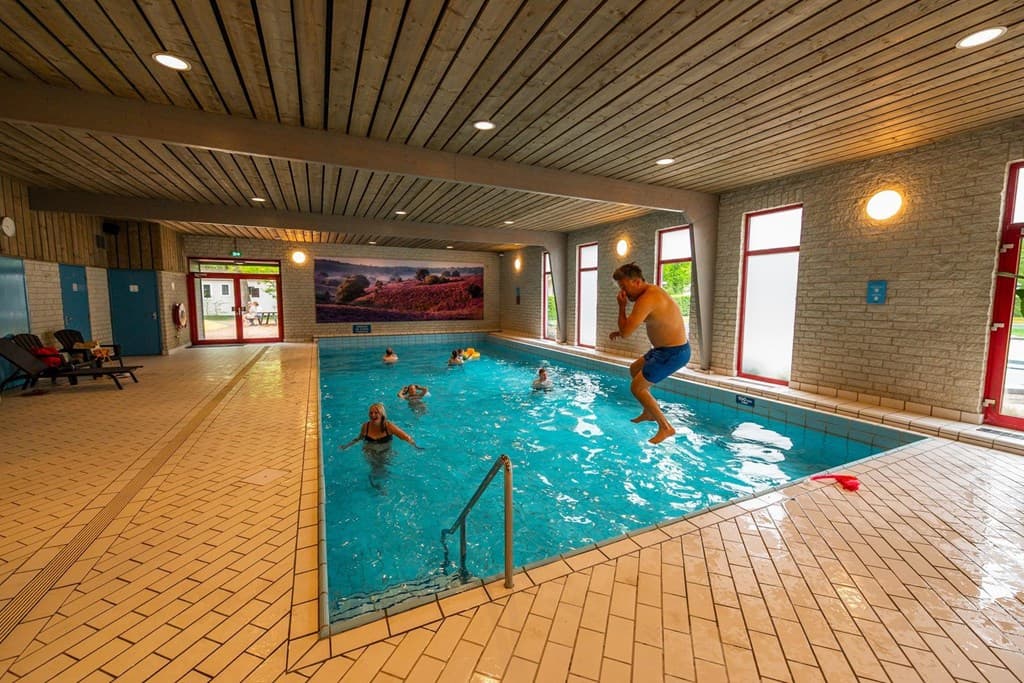 Binnenzwembad met mensen die zwemmen en spelen, houten plafonds en grote ramen voor natuurlijk licht