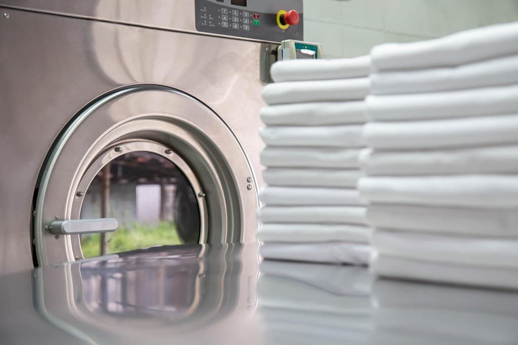 Wasmachine met open deur en een stapel opgevouwen, witte handdoeken ernaast op een metalen tafel