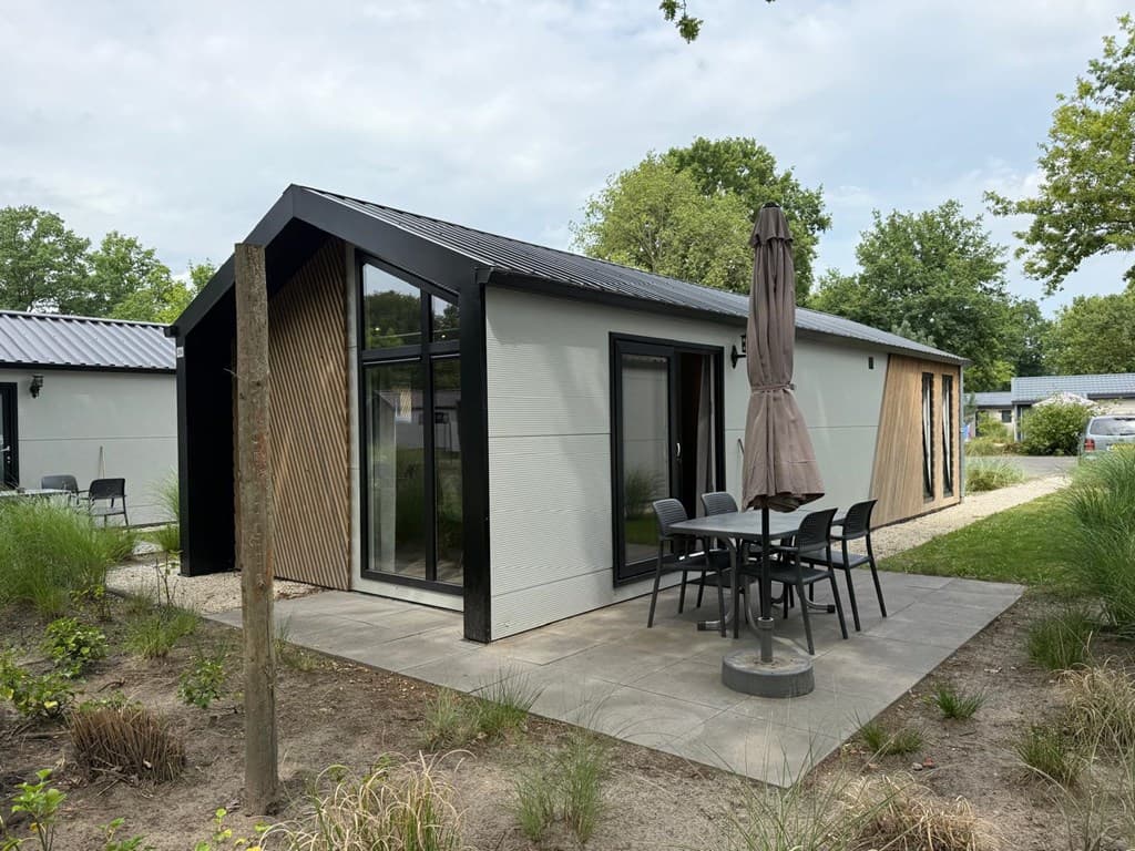Moderne woning met een groot terras, tafel en stoelen, omgeven door groen en bestrating.