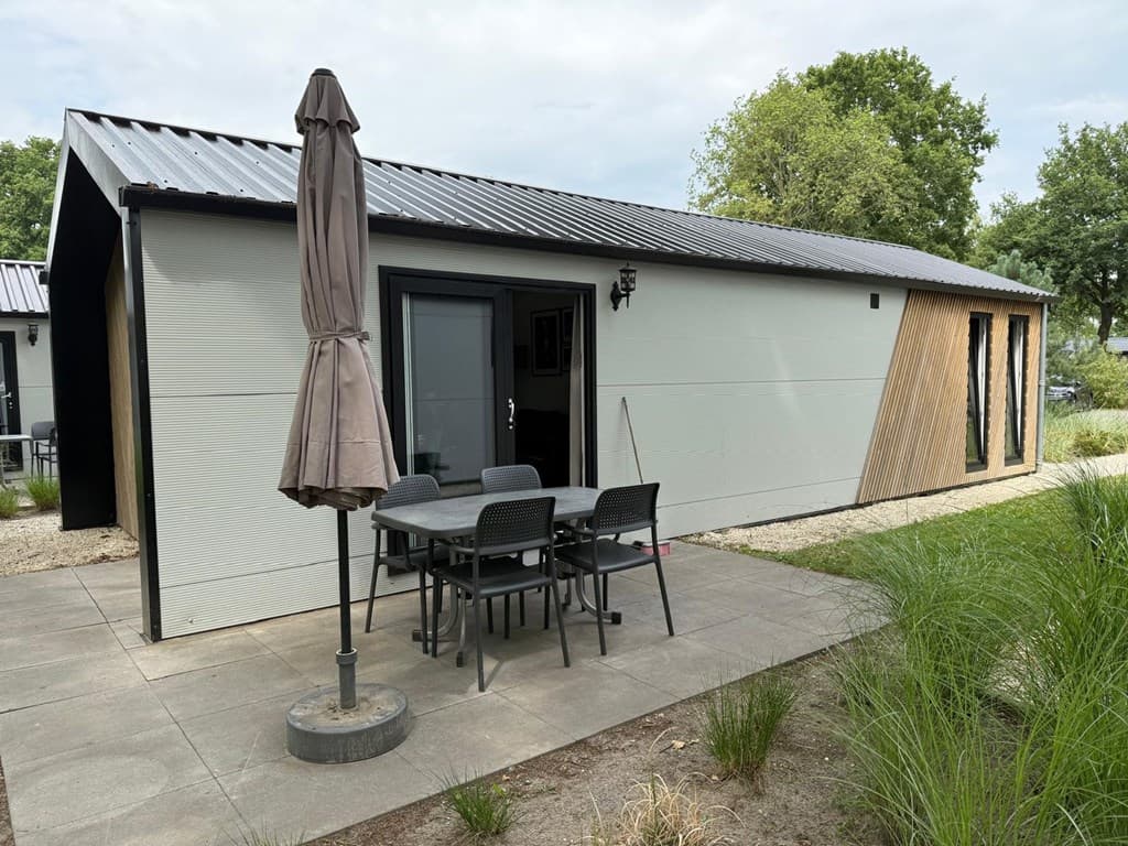 Moderne vakantiewoning met houten accenten, terras en parasol, omringd door groene hagen en gravelpad.
