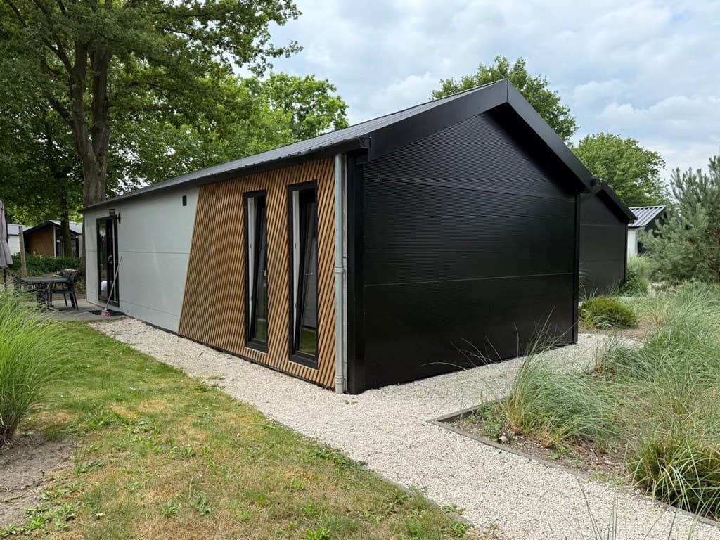Moderne vakantiewoning met een combinatie van zwarte en houten gevel, omringd door groen en grindpaden.