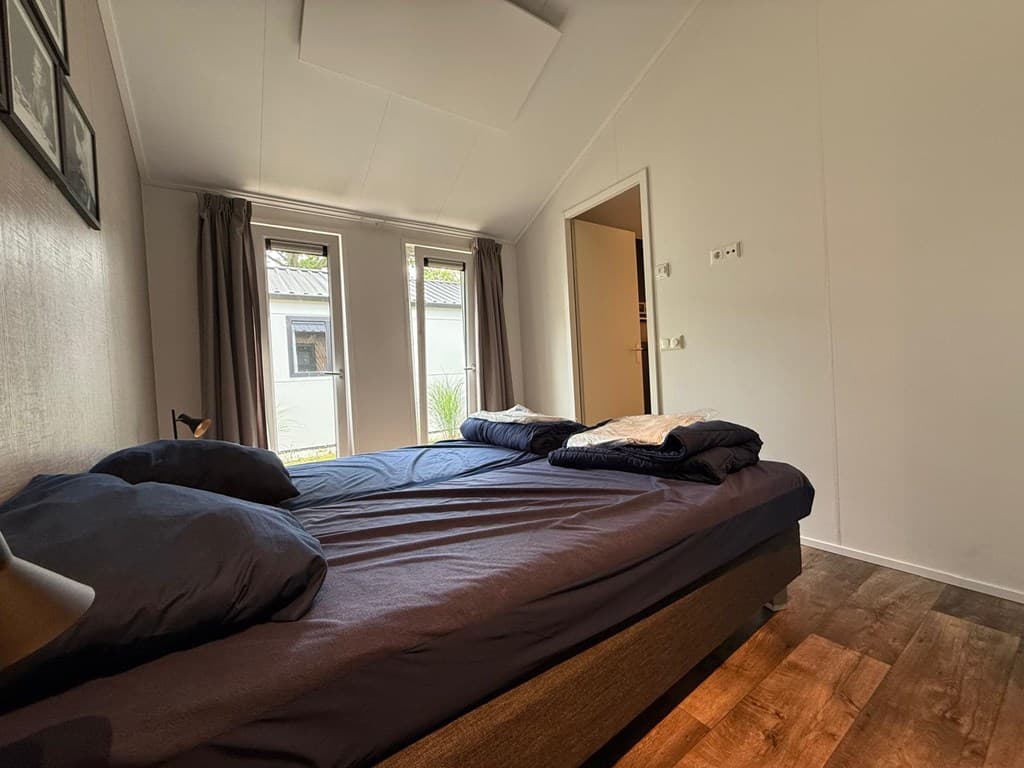 Slaapkamer met een tweepersoonsbed, twee ramen en een deur naar een buitenruimte.
