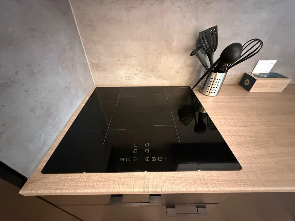Inbouw inductiekookplaat met bedieningsknoppen op een houten aanrecht met kookgerei en keukenaccessoires ernaast.