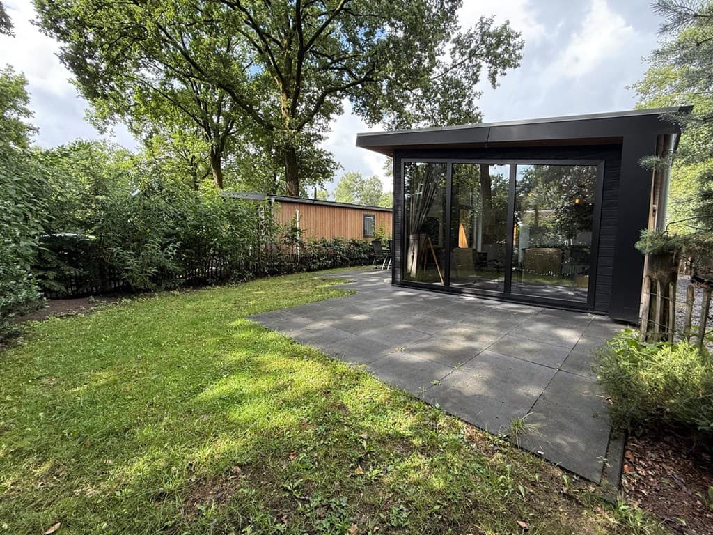 Moderne woning met grote glaspuien, omgeven door groen en een betegeld terras aan de achterkant.