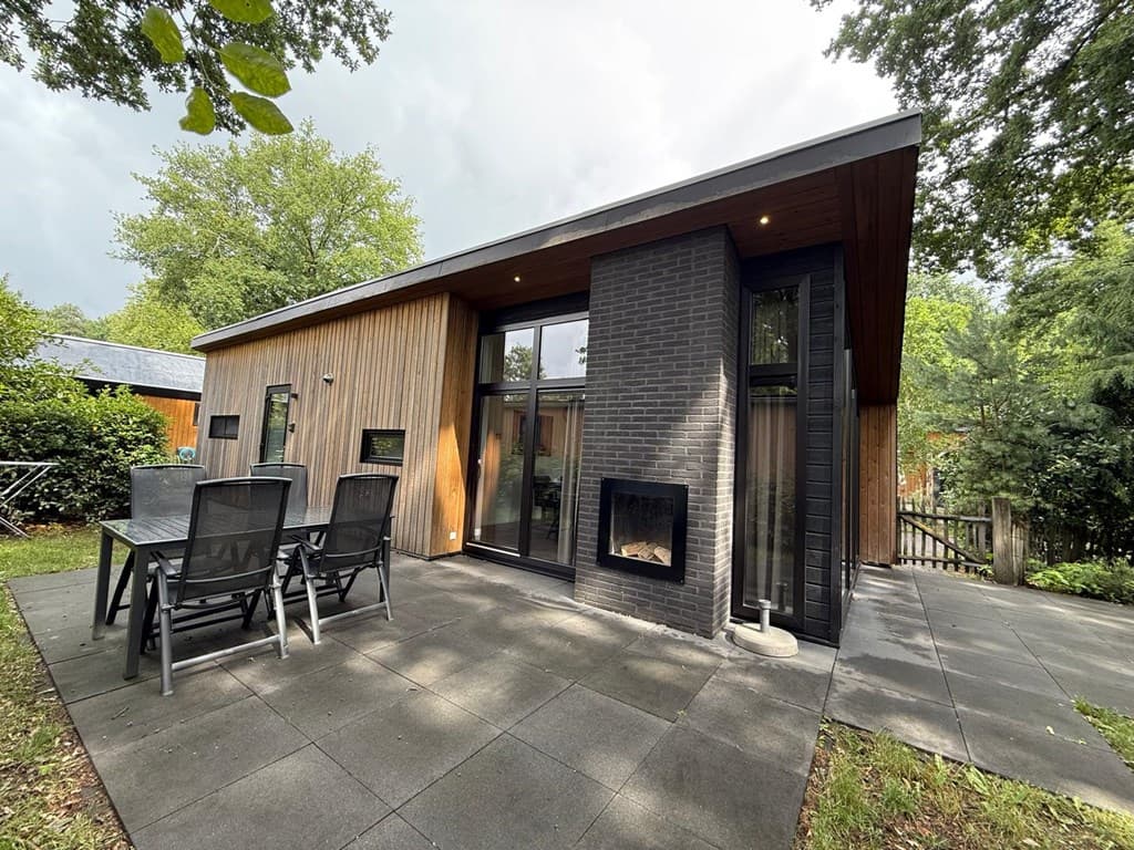 Moderne vakantiewoning met houten gevel en stenen accenten, tuinset op terras en bomen rondom