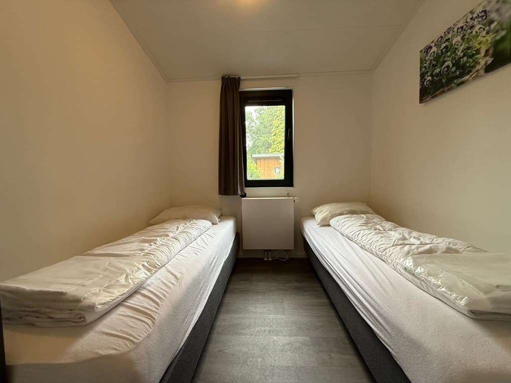 Slaapkamer met twee eenpersoonsbedden, raam met uitzicht op de tuin en eenvoudige wanddecoratie.