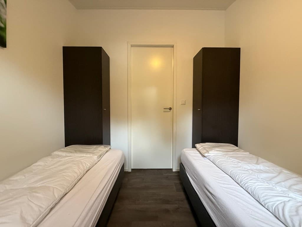 Slaapkamer met twee éénpersoonsbedden en twee donkere kastjes aan weerszijden van de deur.