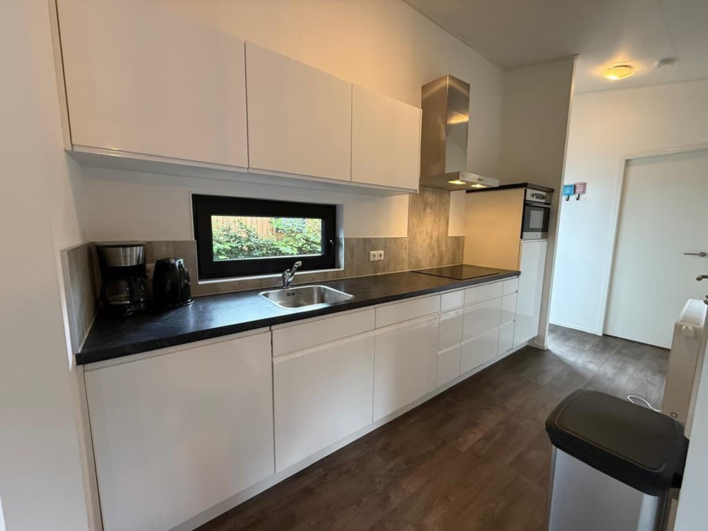 Moderne keuken met witte kasten, zwarte werkblad en ingebouwde apparatuur, inclusief koffiezetapparaat en spoelbak.