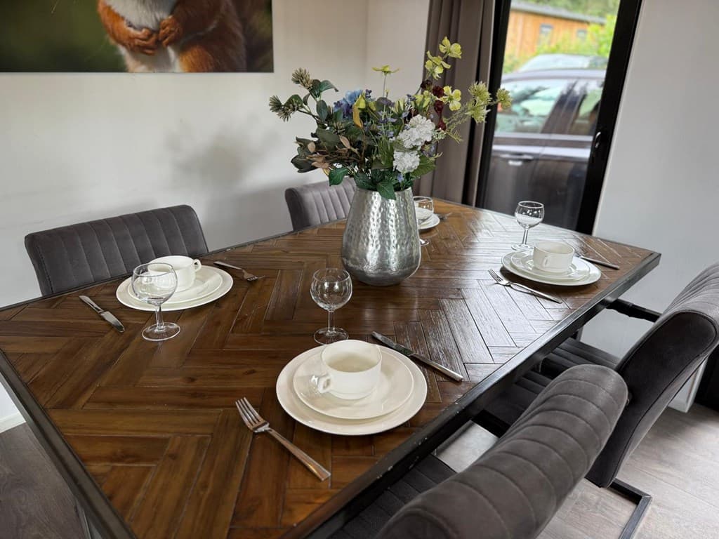 Eettafel met vier stoelen, servies en een vaas met bloemen in een modern interieur.