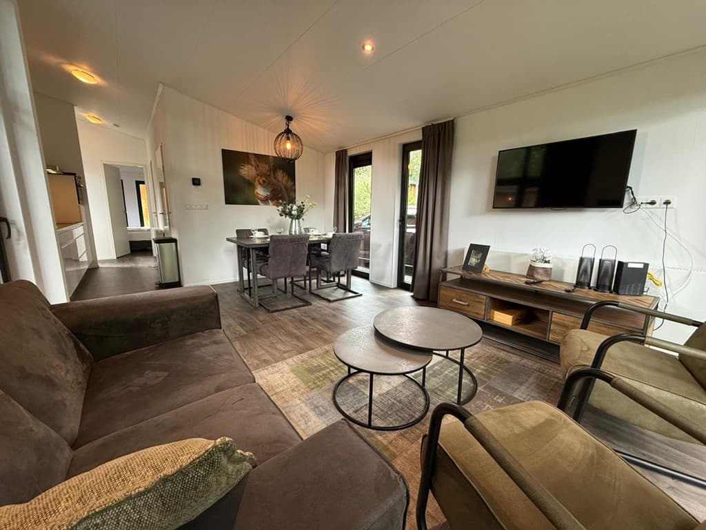 Moderne woonkamer met zitmeubels, eethoek en televisie, grote ramen met uitzicht op buiten.