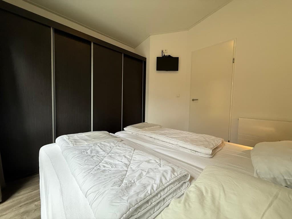Slaapkamer met twee afzonderlijke bedden, donkere kast en wand-tv aan de muur.