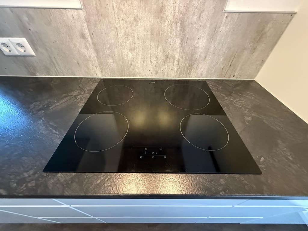 Inductiekookplaat met vier kookzones op een donkere aanrecht in een moderne keuken.