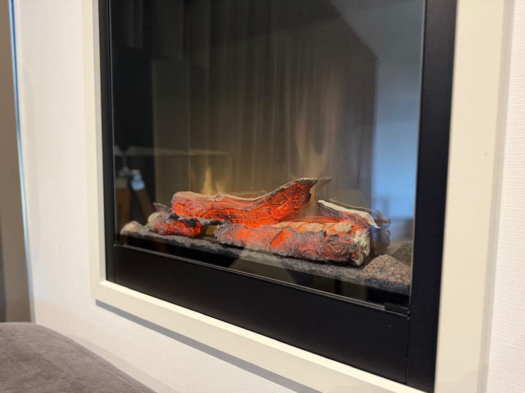 Ingebouwde gashaard met brandende decoratieve houtblokken en kiezels in een moderne omlijsting.