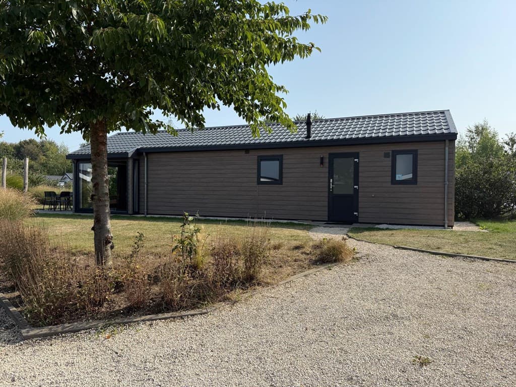 Moderne vakantiewoning met houten gevel, dakpannen en tuin met gras en struiken.