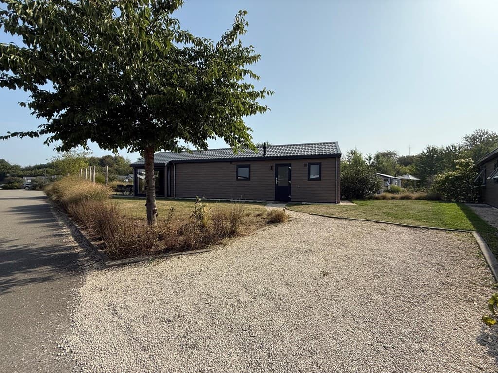 Zicht op een vakantiewoning met een tuin en een grindpad, omringd door enkele bomen en groen.