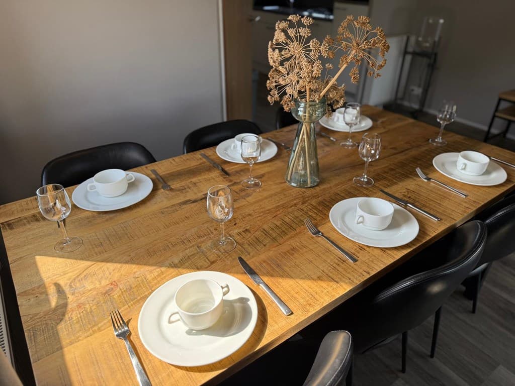 Eettafel met servies en glazen, zwart-lederen stoelen, en een vaas met gedroogde takken als decoratie.
