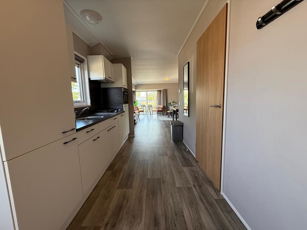 Keukenruimte met lichtgekleurde kasten, toegang tot een open woonkamer met uitzicht op het terras.