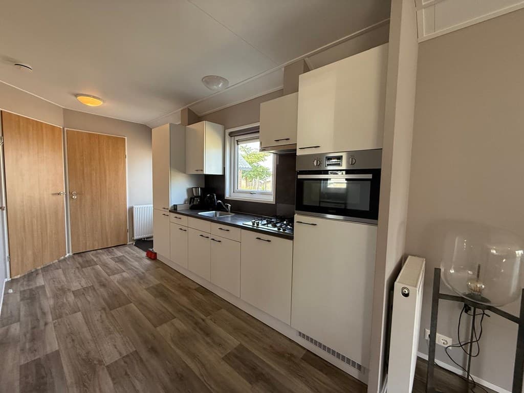 Moderne keuken met witte kasten, een oven, kookplaat en raam met uitzicht op buiten, vloeren van laminaat.