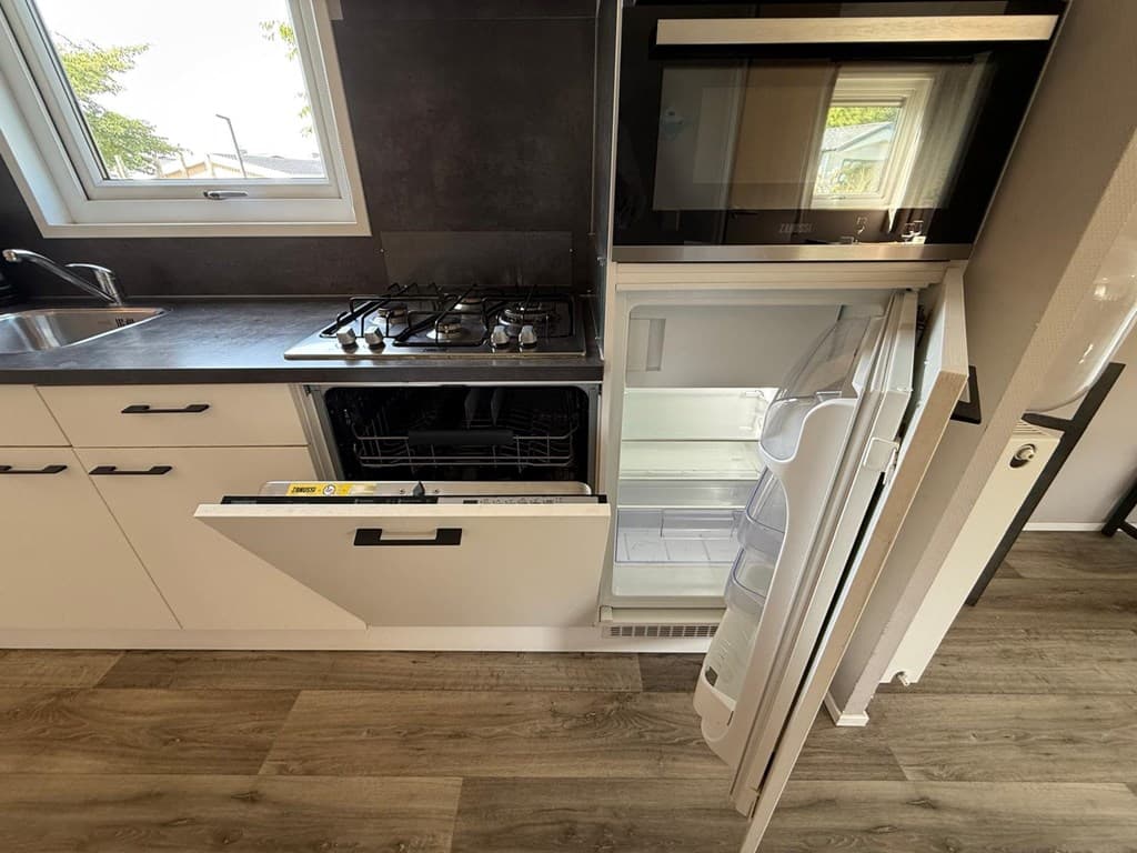 Moderne keuken met inbouwapparatuur, waaronder een kookplaat, oven en koelkast met vriezer, en een afwasmachine.